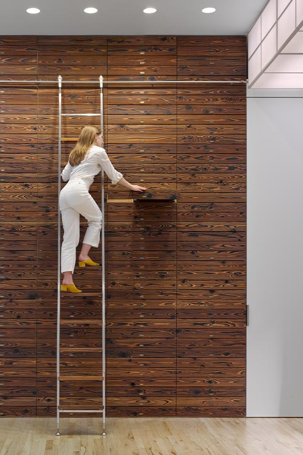 person on ladder climbing up wall of wooden drawers